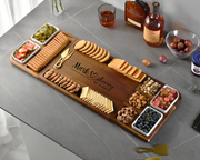 A wooden serving platter with various snacks and crackers, including crackers, grapes, and cheese, along with a bottle of whiskey and other condiments.